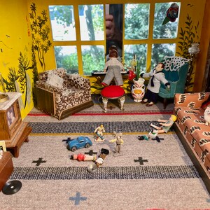May include: A dollhouse living room with a yellow wall, a window with a view of trees, a brown armchair, a red ottoman, a blue car, and several toy figures on a gray and white striped rug.
