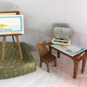 Puede incluir: Un caballete de madera en miniatura con una pintura de acuarela de un paisaje mar&iacute;timo, un peque&ntilde;o escritorio de madera con una silla, un juego de pintura de acuarela y un pincel.