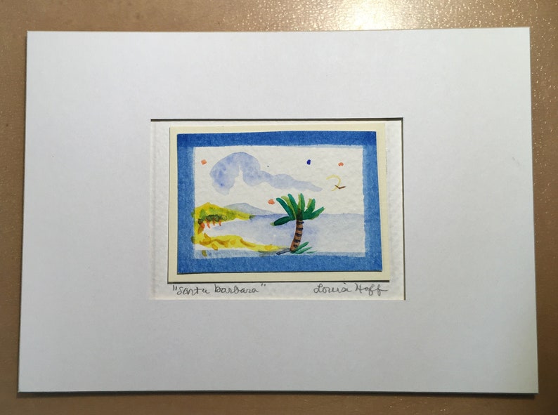 Puede incluir: Una pintura de acuarela de una escena de playa con una palmera, cielo azul y nubes. La pintura est&aacute; enmarcada y firmada "Santa Barbara" por "Louisa Hoff".