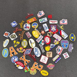 May include: A collection of colorful enamel pins and patches with various designs and text. The pins feature logos, text, and graphics, including the letters "A" and "X", and the words "Success Rice" and "Science Diel".