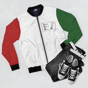 Pu&ograve; includere: Giacca bomber bianca con maniche rosse e verdi, cerniera nera e colletto nero. La giacca presenta la scritta "Little Nero's Pizza" con un personaggio dei cartoni animati. Abbinata a jeans scuri e scarpe da ginnastica nere.