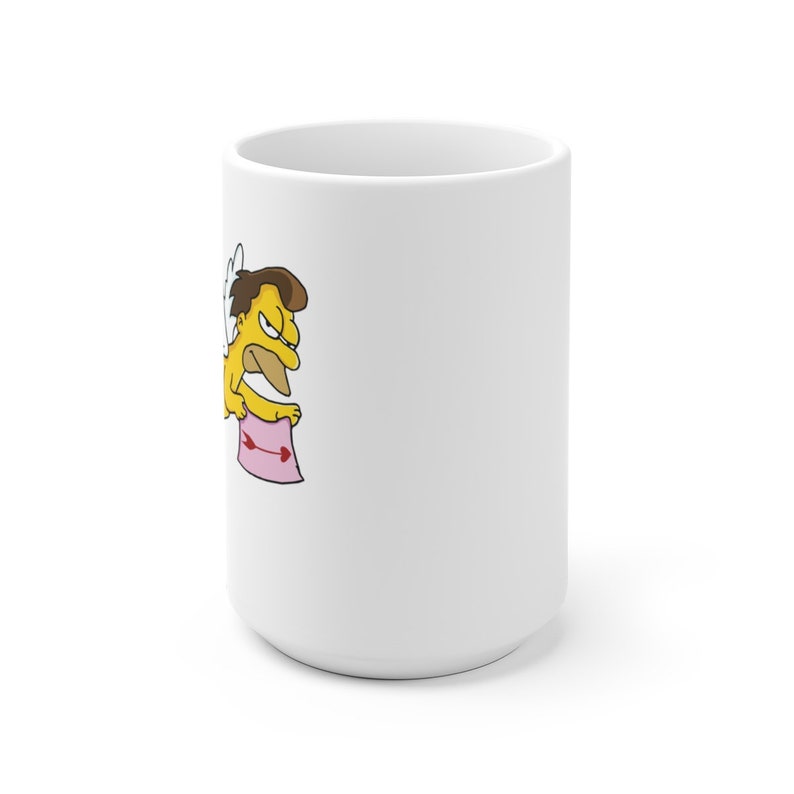 May include: White ceramic mug with a cartoon image of a yellow character with brown hair, wings, and a pink arrow. The character is holding a pink sign with a red arrow.