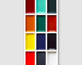 May include: A white rectangular shelf with twelve rectangular compartments, each filled with a different solid color. Colors include red, teal, dark green, orange, yellow, blue, and black.