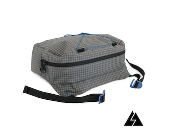 May include: A gray and black rectangular bag with a zipper closure and a blue strap. The bag has a grid pattern and a blue drawstring.