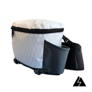 Könnte beinhalten: Eine weiße und schwarze Bauchtasche mit einem Reißverschlussfach und einer kleineren Seitentasche. Die Tasche hat ein Rautenmuster auf der Vorderseite und einen schwarzen Gurt.