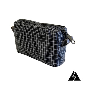 May include: A black zippered pouch with a grid pattern and a black zipper pull. The pouch has a grey strap.