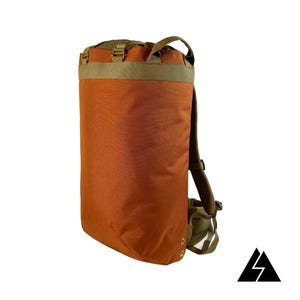 Könnte beinhalten: Ein hoher, orangefarbener Rucksack mit Rollverschluss und olivgrünen Akzenten. Der Rucksack hat verstellbare Träger und einen oberen Griff. Ein schwarz-weißes Logo befindet sich in der unteren rechten Ecke.