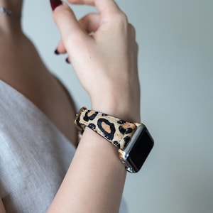 May include: A close-up of a person's wrist wearing a smartwatch with a leopard print band. The watch face is black and the band is brown and black.