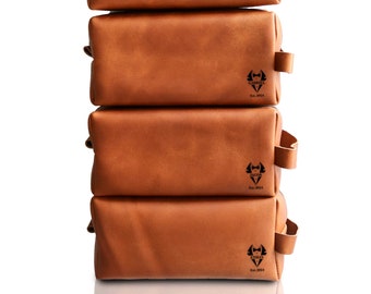 May include: Six brown leather toiletry bags stacked on top of each other. Each bag has a black logo with a stylized beard and the text "Lucas Est. 2014".