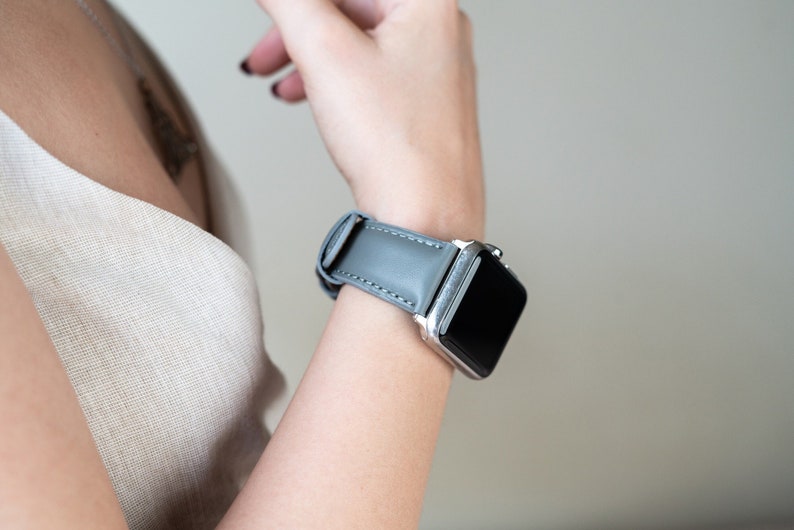 May include: A gray leather watch band with a silver watch face.