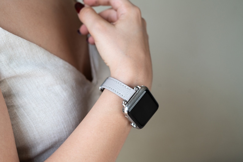 May include: A light gray leather watch band with a silver smartwatch. The watch face is black and the band has a subtle texture.