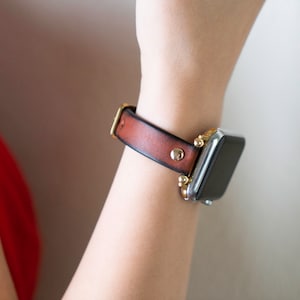 Op de afbeelding: Een bruin leren horlogebandje met gouden accenten en een zilveren smartwatch.