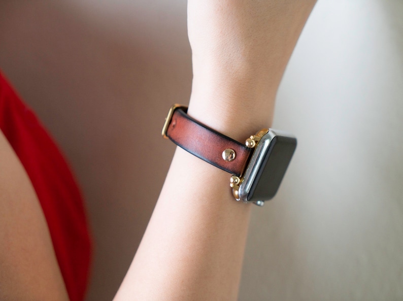 Op de afbeelding: Een bruin leren horlogebandje met gouden accenten en een zilveren smartwatch.