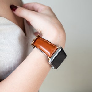 May include: A brown leather watch band with a silver watch face. The watch band is on a person's wrist.