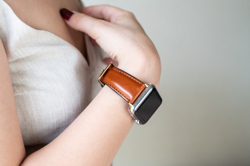 May include: A brown leather watch band with a silver watch face. The watch band is on a person's wrist.