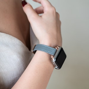 May include: A gray leather watch band with rose gold accents and a black watch face.