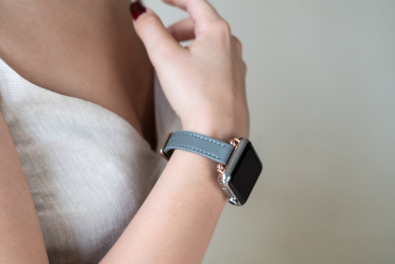 May include: A gray leather watch band with rose gold accents and a black watch face.