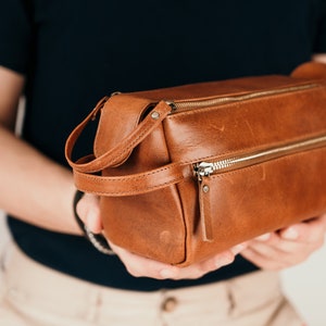 May include: A brown leather travel wash bag with a zip fastening and a carrying handle.