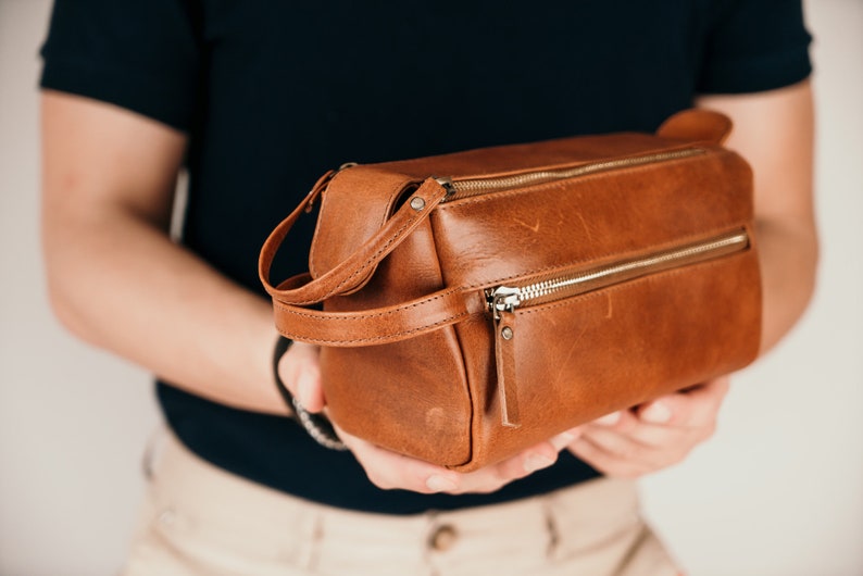 May include: A brown leather travel wash bag with a zip fastening and a carrying handle.