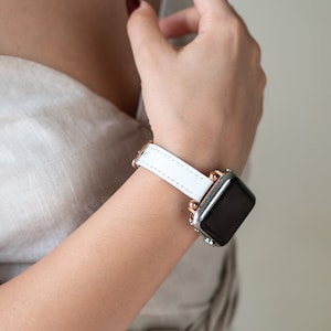 May include: A white leather watch band with rose gold accents on a silver smartwatch.