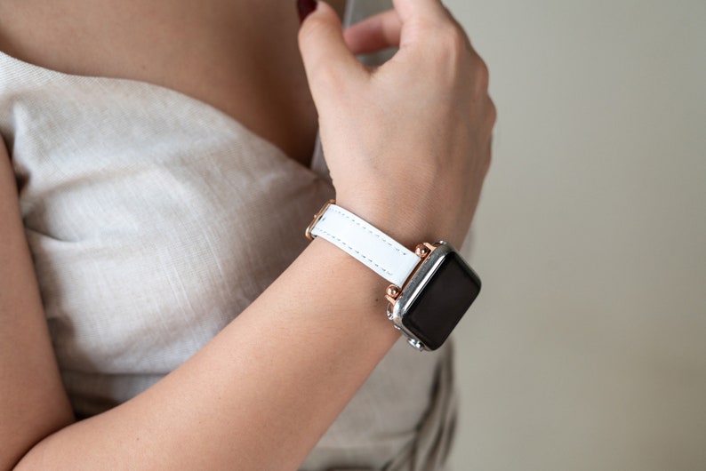 May include: A white leather watch band with rose gold accents on a silver smartwatch.