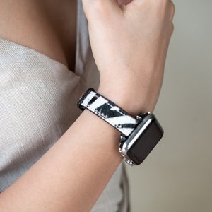 May include: A black and white zebra print watch band with a silver watch face.