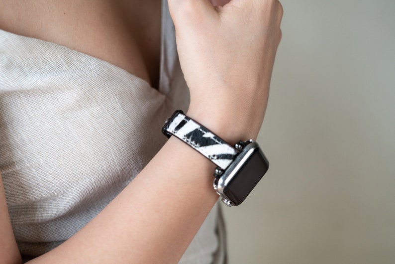 May include: A black and white zebra print watch band with a silver watch face.