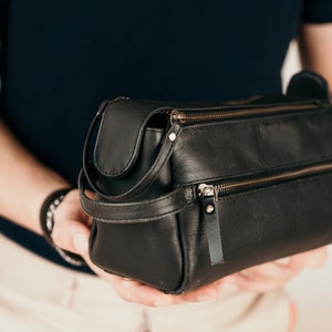 May include: A black leather travel wash bag with a zip closure and a gold zip pull.