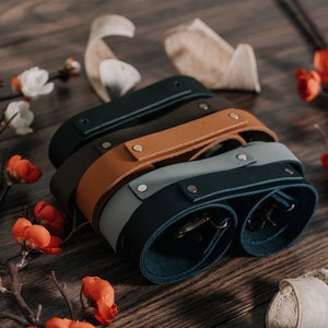 May include: Four leather camera straps in different colors: dark blue, light blue, brown, and black. The straps are stacked on top of each other and have metal hardware.