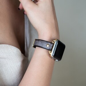 Op de afbeelding: Een bruin leren horlogebandje met gouden accenten op een zilveren smartwatch.