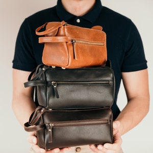 May include: A stack of three leather travel bags. The top bag is brown, the middle bag is black, and the bottom bag is dark brown.
