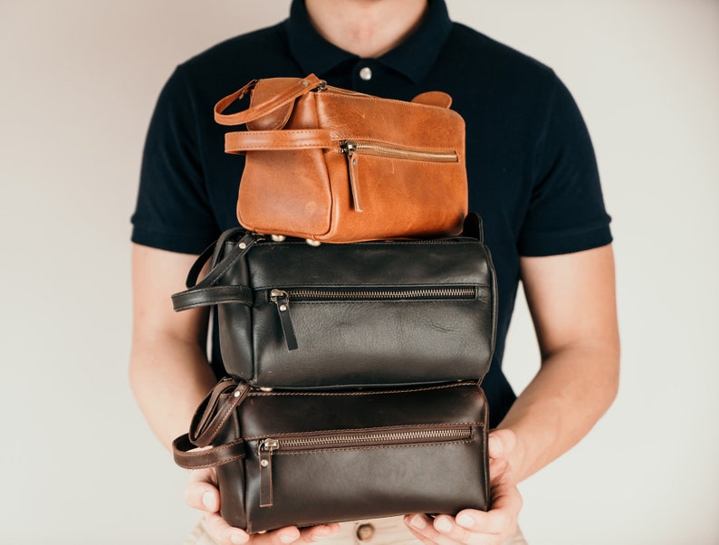 May include: A stack of three leather travel bags. The top bag is brown, the middle bag is black, and the bottom bag is dark brown.
