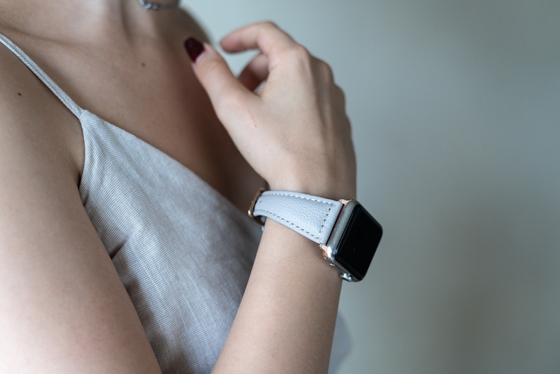 May include: A light gray leather watch band with a rose gold buckle and a silver Apple Watch.