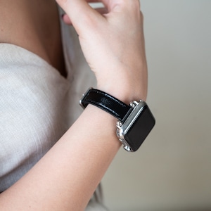May include: A black leather watch band with a silver watch face. The watch band has a silver buckle.