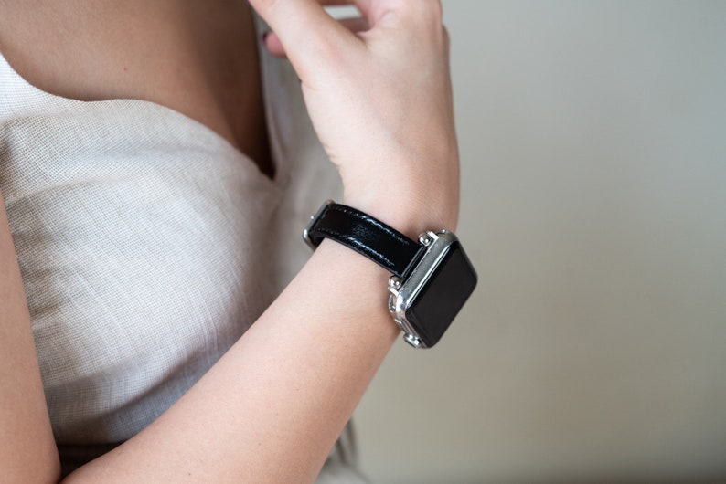 May include: A black leather watch band with a silver watch face. The watch band has a silver buckle.