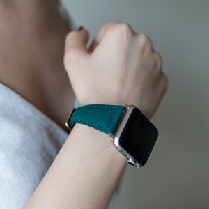 May include: A teal leather watch band with a rose gold buckle and a silver smartwatch.