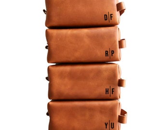 May include: A stack of six brown leather toiletry bags with personalized initials. The initials are E|C, D|F, R|P, H|F, Y|U, and K|L.
