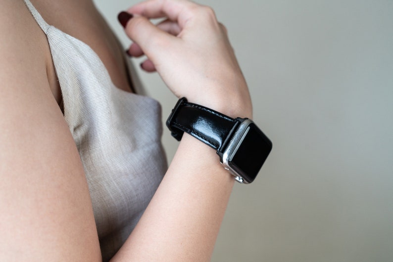May include: A black leather watch band with a silver watch face. The band is shiny and has a smooth texture.