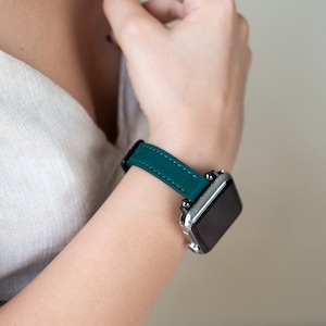 May include: A teal leather watch band with a silver watch face.