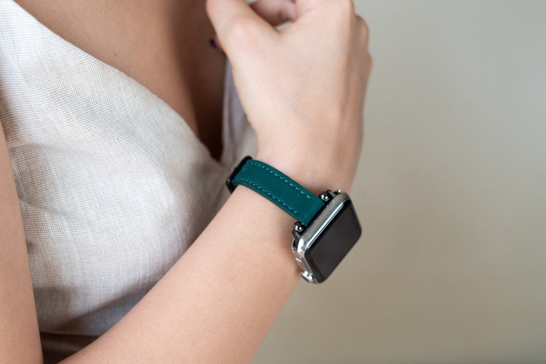 May include: A teal leather watch band with a silver watch face.