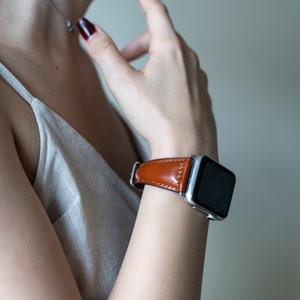 May include: A brown leather watch band with a silver watch face. The watch is on a person's wrist.