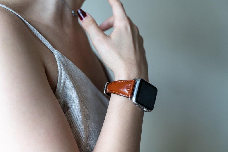May include: A brown leather watch band with a silver watch face. The watch is on a person's wrist.