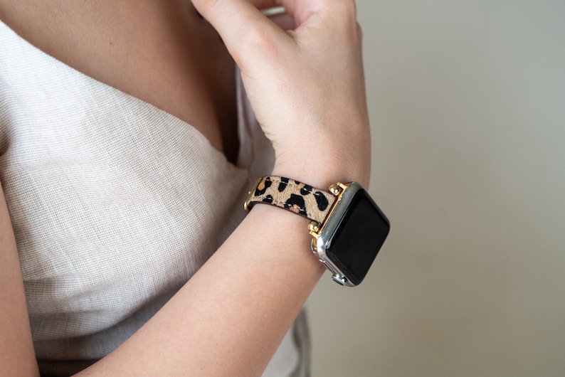 May include: A silver and gold Apple Watch with a black screen and a leopard print band.
