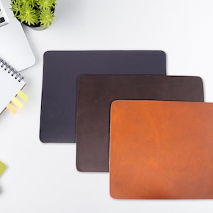 May include: Three leather desk mats in different colors: dark gray, brown, and orange. The orange mat has the letters "B/N" in black.