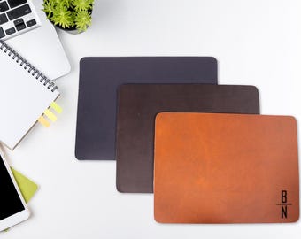 May include: Three leather desk mats in different colors: dark gray, brown, and orange. The orange mat has the letters "B/N" in black.