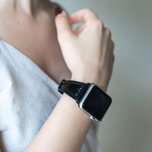 May include: A silver smartwatch with a black leather band. The watch face is black and the band is smooth.
