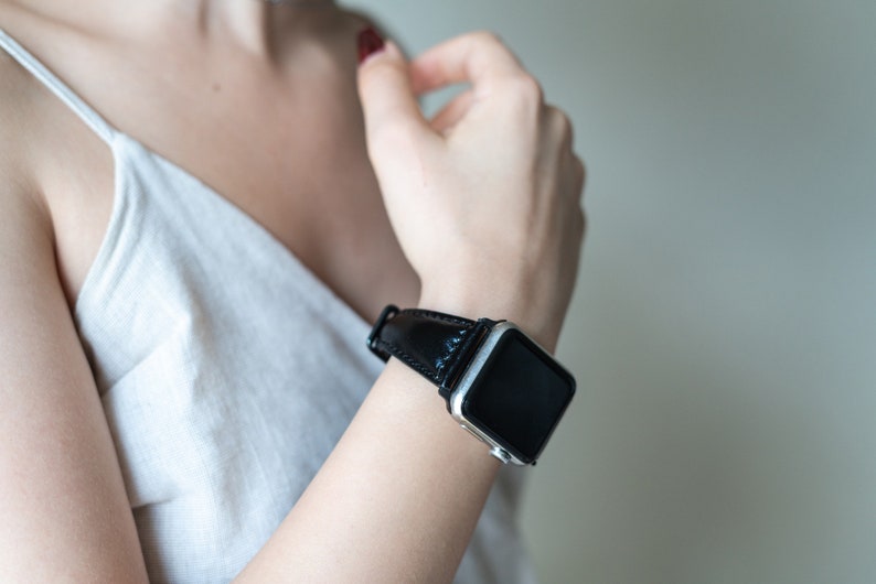 May include: A silver smartwatch with a black leather band. The watch face is black and the band is smooth.