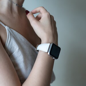 May include: A white leather watch band with a silver watch face. The watch is on a person's wrist.