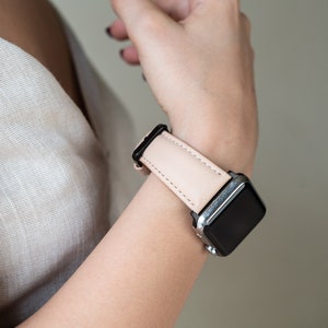 May include: A blush pink leather watch band with a silver Apple Watch.