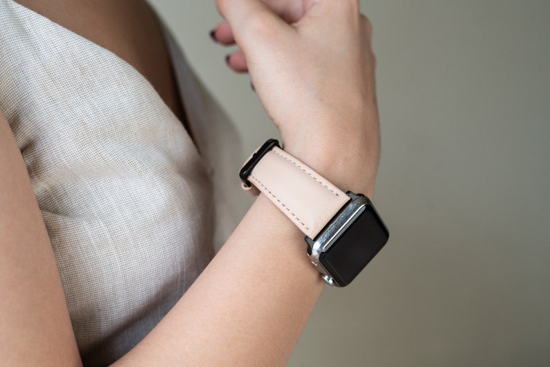 May include: A blush pink leather watch band with a silver Apple Watch.
